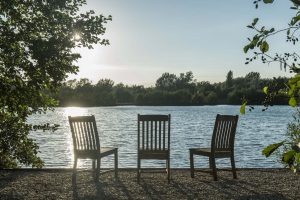 3 wooden outdoors chairs at edge of the lake near Island Lodge